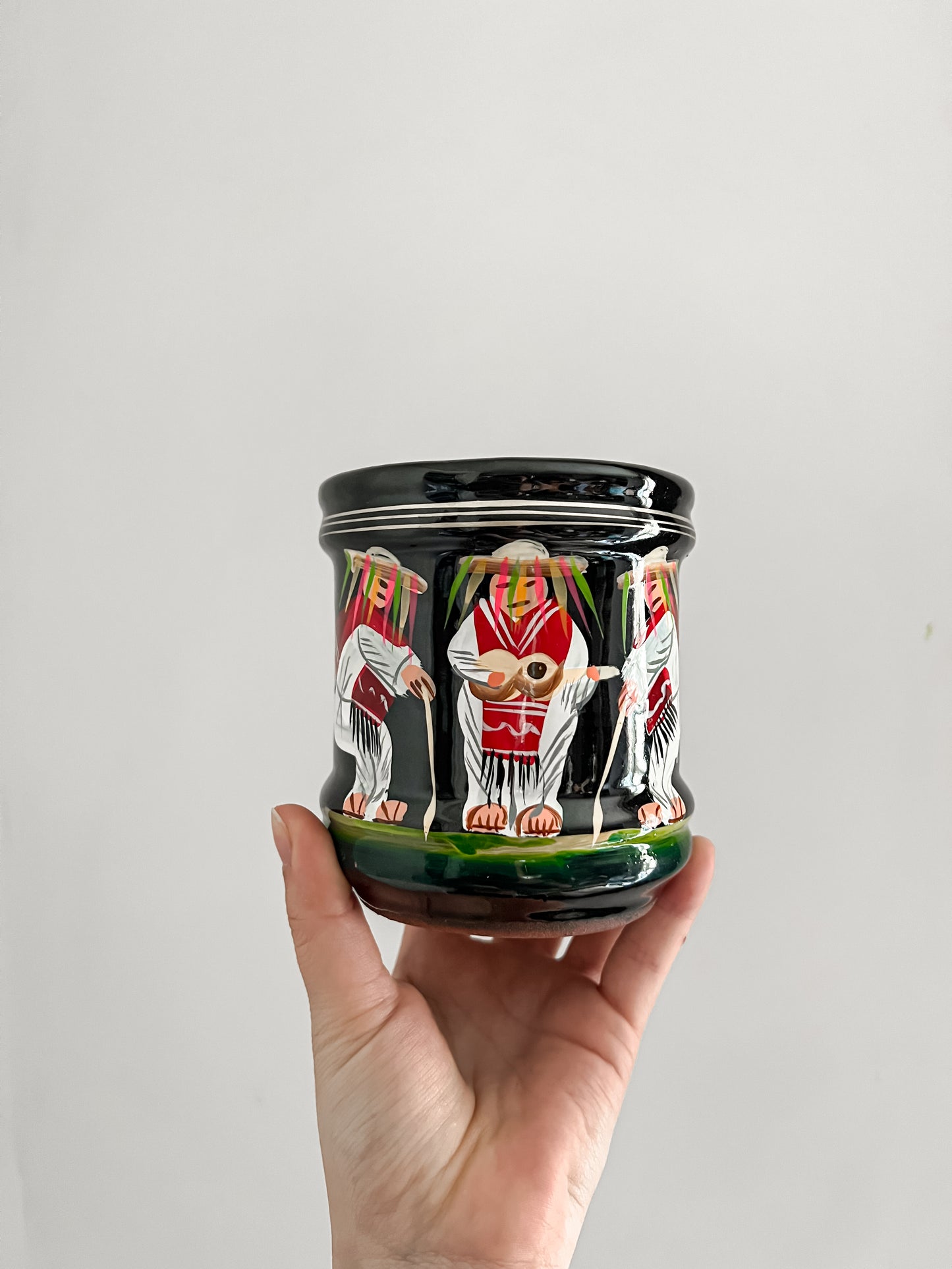 Hand holding a decorative jar with painted figures on a plain background